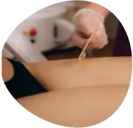 Close-up of a hand applying wax to a person's bare back with a spatula.