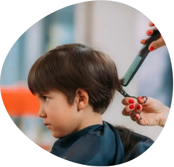 Child getting a haircut as a stylist combs the hair with scissors nearby