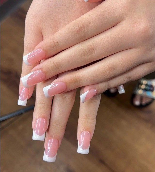 Hands with long pink-and-white French manicure nails crossed over a wooden floor.
