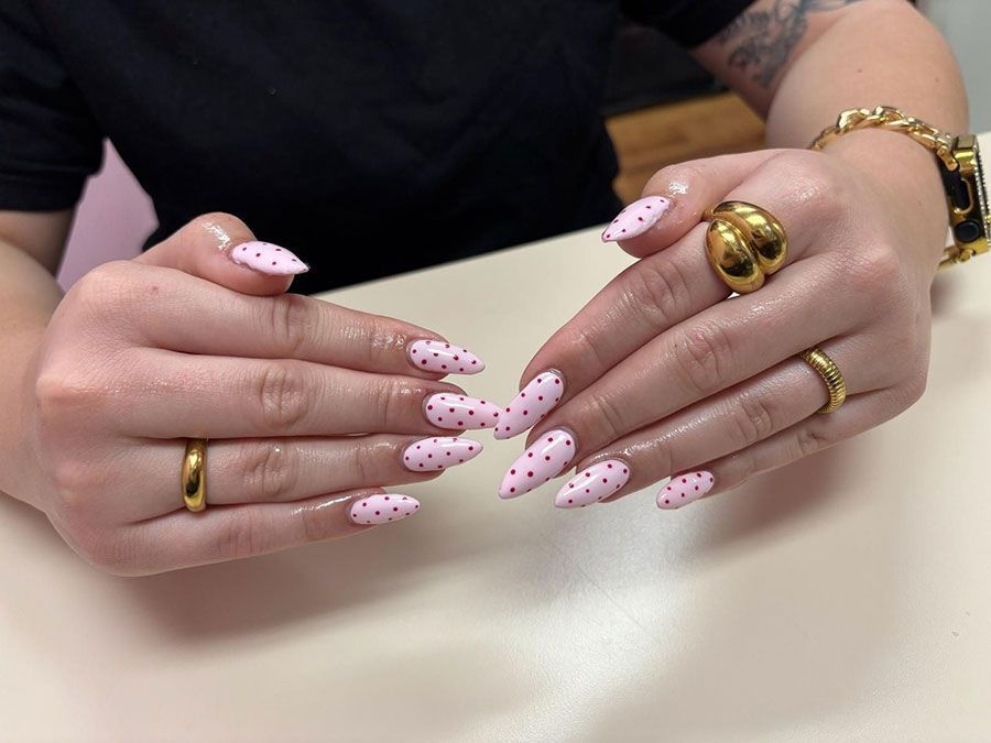Hands with long pink polka-dot nails and gold rings resting on a table