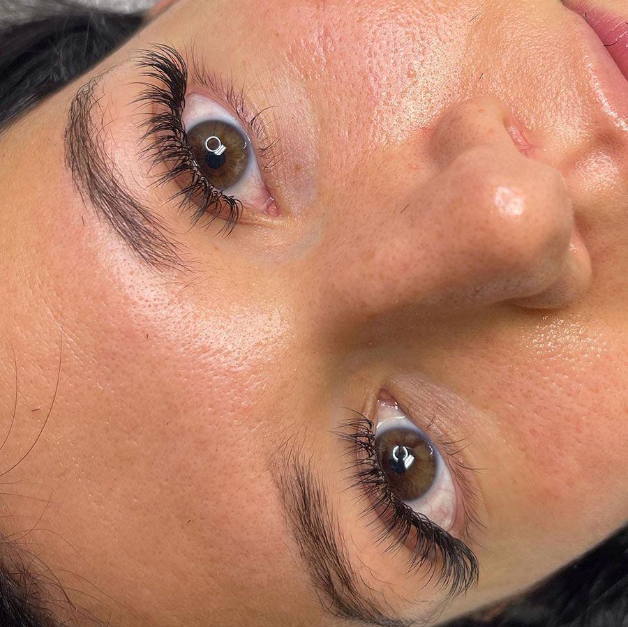 Close-up of a face with brown eyes and long lashes, rotated sideways against a pink background