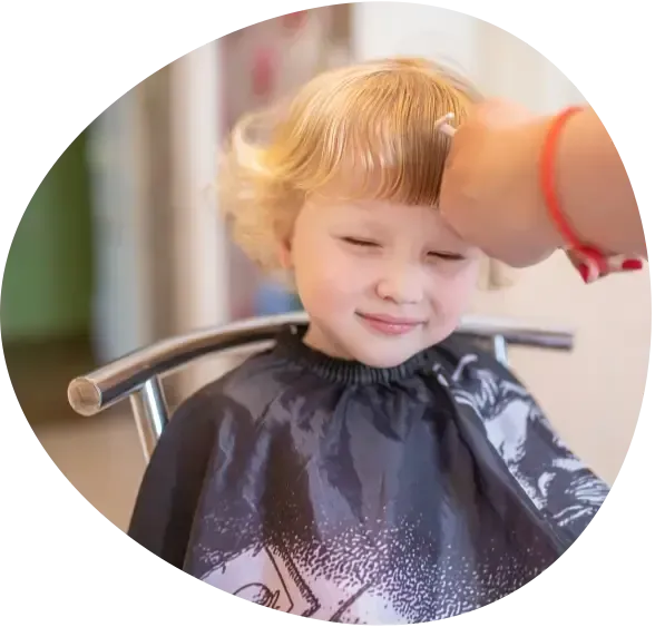 Child with closed eyes getting a haircut under a black salon cape