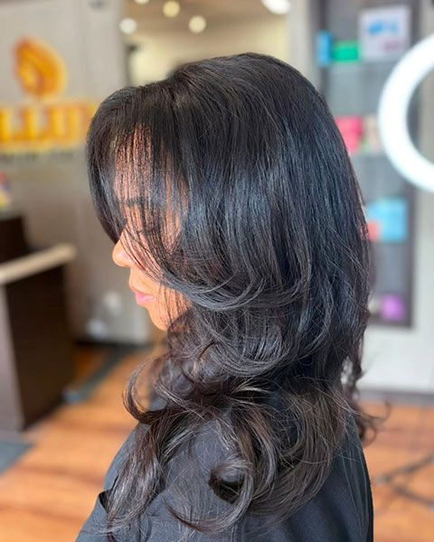 Side view of layered wavy dark hair with silver highlights in a salon setting