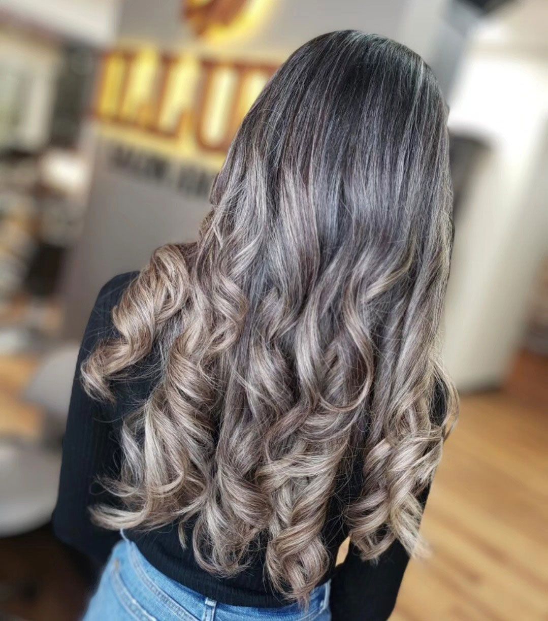 Long wavy brown hair with blonde highlights, viewed from behind in a salon setting