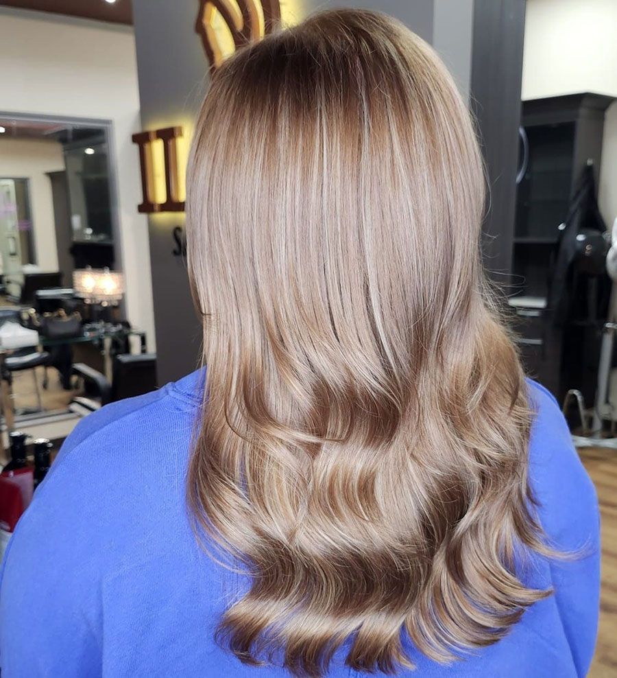 Back view of long, wavy blonde hair with darker roots in a salon
