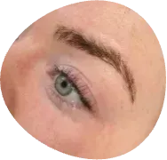 Close-up of a green eye with subtle purple eyeshadow and a brown eyebrow