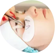 Close-up of eyelash extension application on a reclining person with tweezers and tape