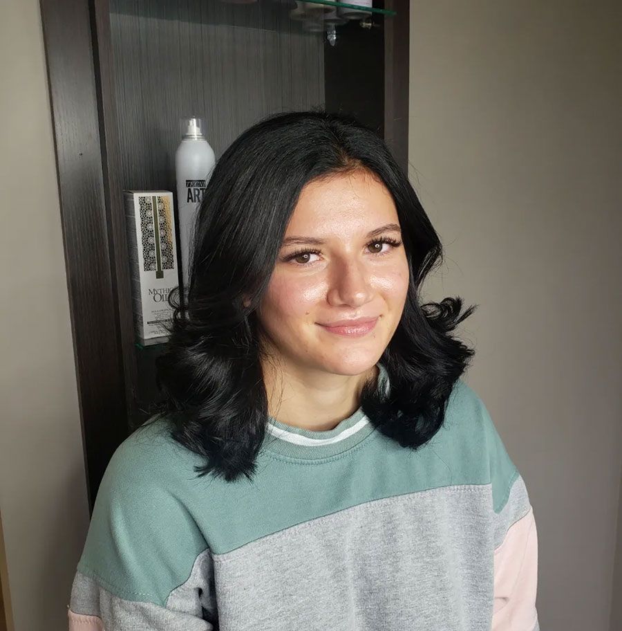 Smiling person with shoulder-length dark hair wearing a mint green sweater indoors