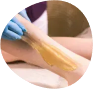 Gloved hand applying warm wax to a person’s leg during a hair removal treatment