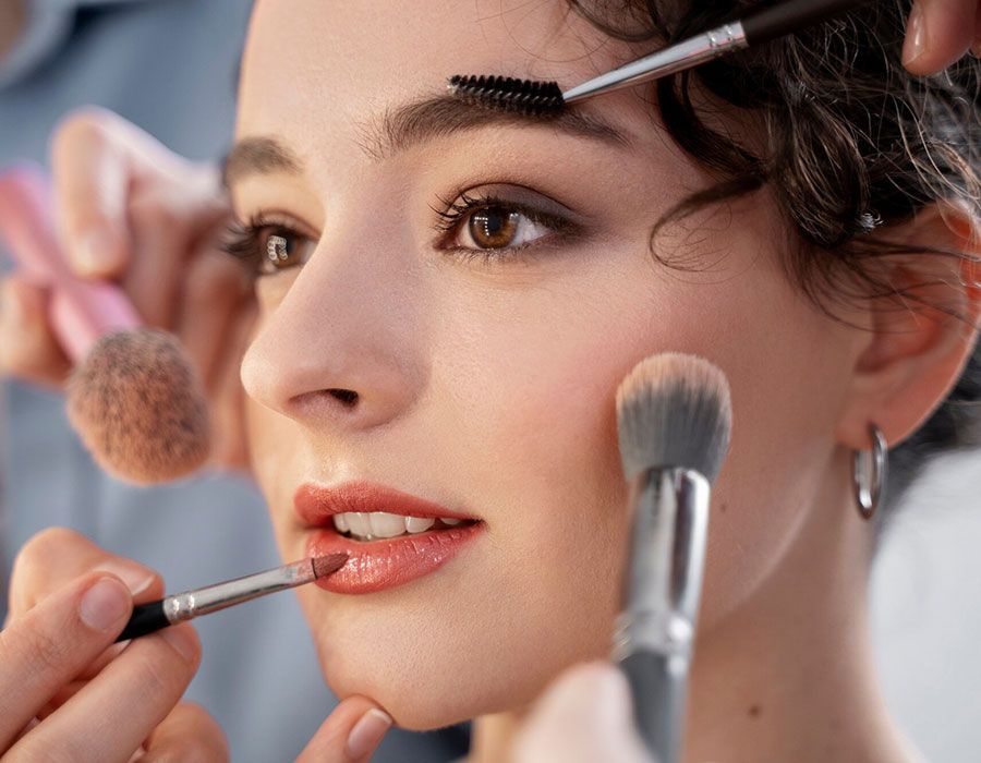 Makeup artist applying makeup to a woman with brushes near her eyes and lips