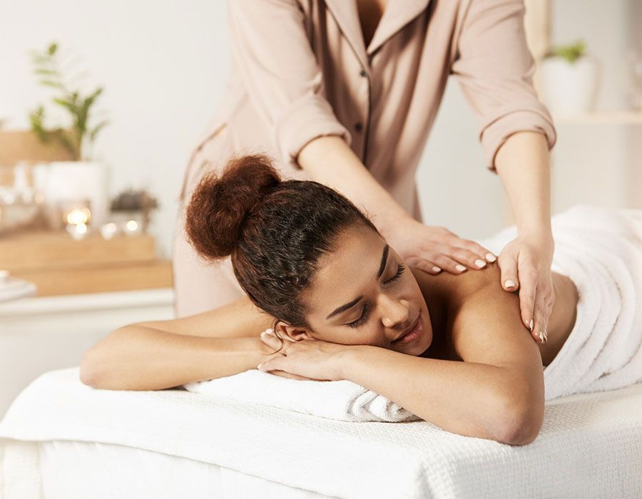 Woman receiving a back massage on a white spa bed in a bright treatment room