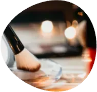 Makeup brush applying powder on a palette, with a blurred cosmetic scene in the background