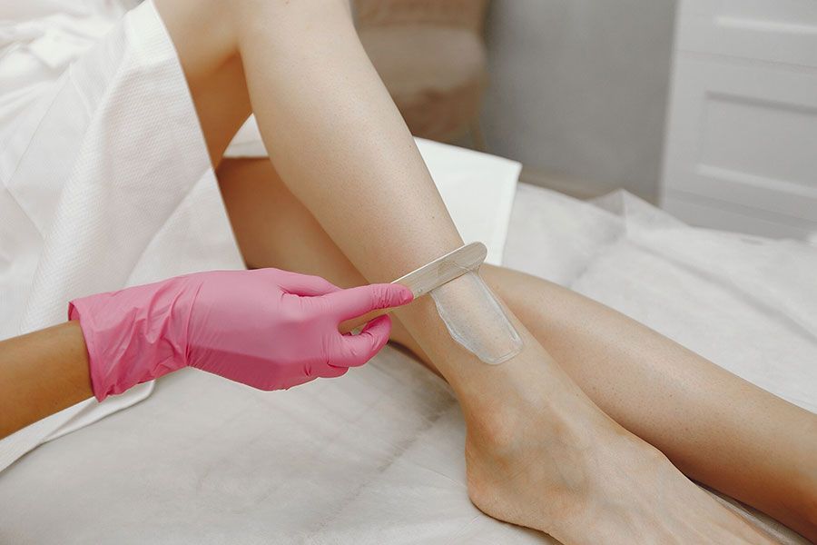 Gloved hands waxing a person’s leg in a spa setting