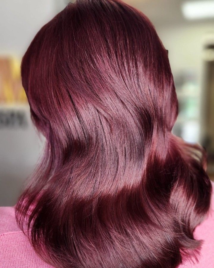 Shiny wavy burgundy hair cascading down the back against a blurred indoor background