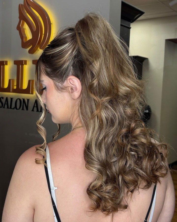 Woman with curly half-up hairstyle, showing blonde highlights and spiral curls, in a salon.
