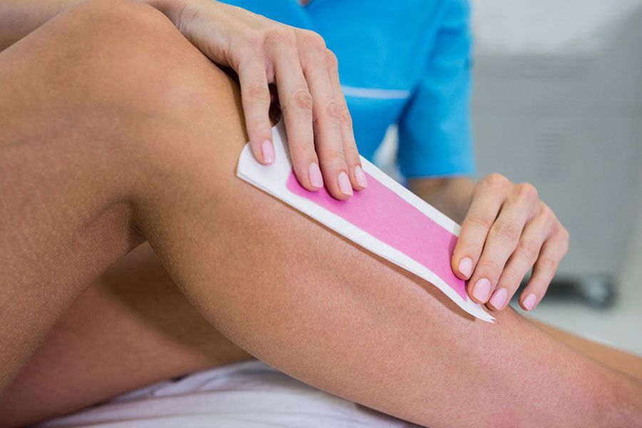 Person waxing a leg with a pink strip in a spa setting