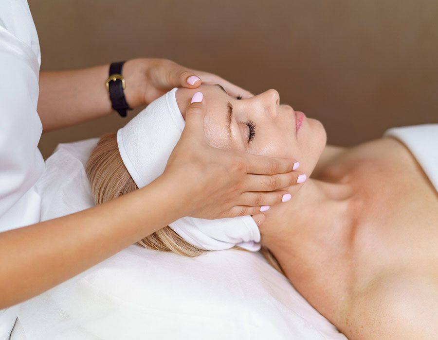 Facial massage at a spa, with hands gently supporting a woman&rsquo;s face on a treatment bed