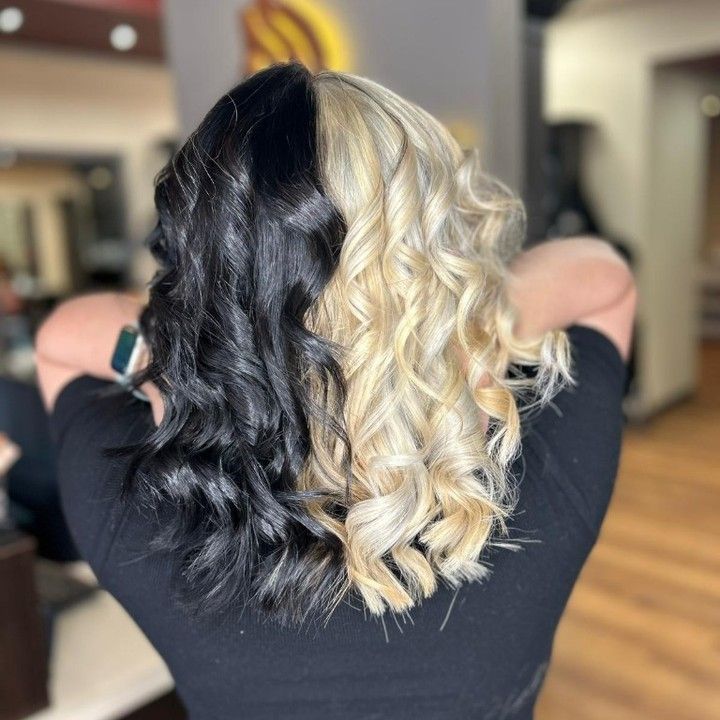 Back view of wavy hair split half black, half blonde in a salon setting