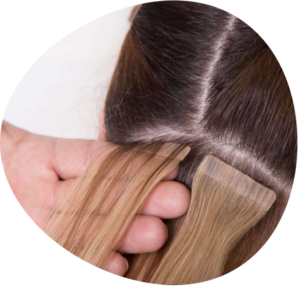 Hands attaching blonde hair extensions to dark hair at the scalp parting