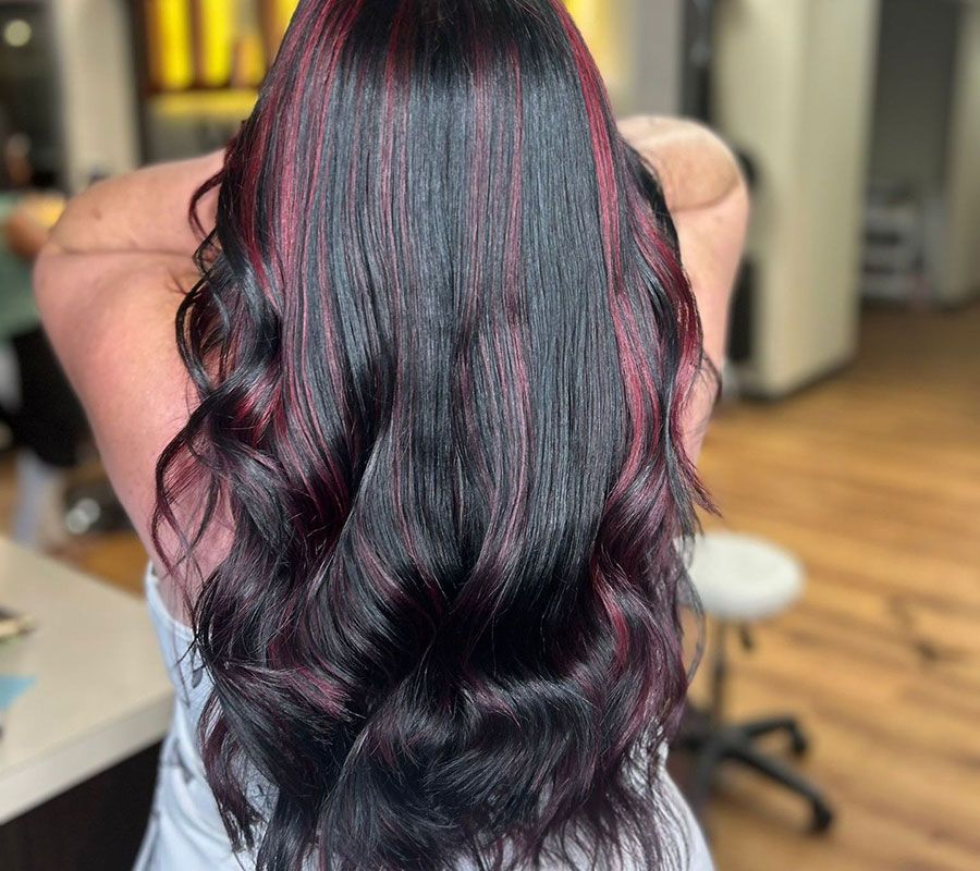 Dark wavy hair with burgundy highlights, viewed from behind in a salon chair