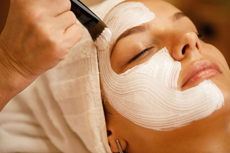 Woman receiving a white facial mask application with a brush at a spa