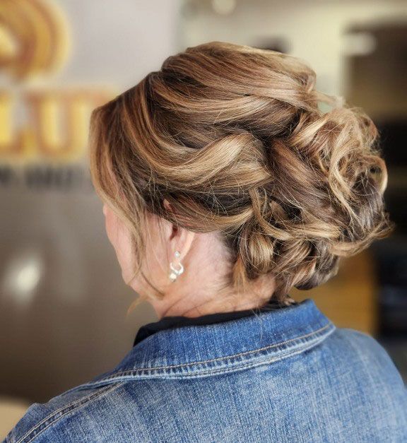 Braided updo hairstyle from the back, shown over a denim jacket, in a salon setting