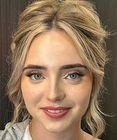 Close-up portrait of a smiling person with blonde hair and blue eyes against a neutral background