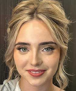 Close-up portrait of a smiling person with blonde hair and blue eyes against a neutral background
