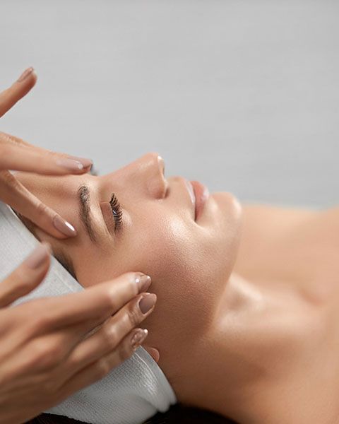 Hands giving a facial massage to a person lying on a spa bed with a white towel.