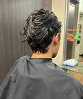 Person with wet, styled dark hair seen from behind in a salon chair, wearing a black cape.