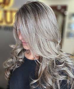 Silver blonde layered curls with side-swept bangs on a dark top