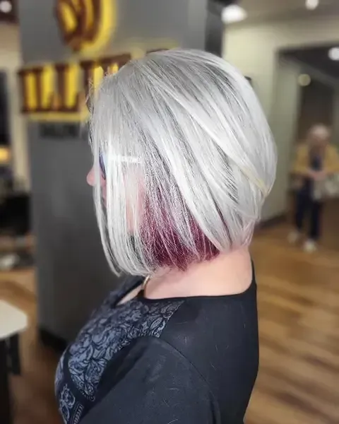 Silver bob haircut with a magenta underlayer, shown in profile in a salon.