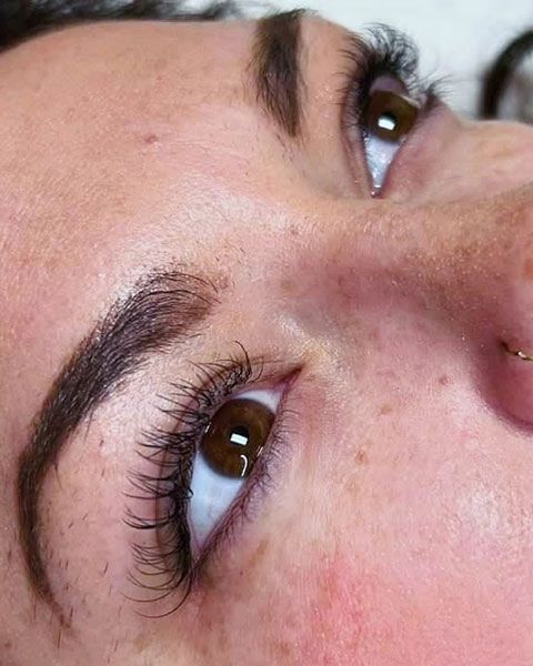 Close-up of a person’s eyes with long curled lashes and neatly shaped eyebrows, looking upward