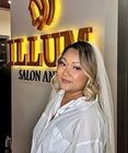 Woman in white blouse posing in a salon lobby beside a glowing gold sign.