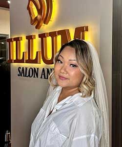 Woman in white blouse posing in a salon lobby beside a glowing gold sign.