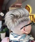 Person with short silver undercut hairstyle and black glasses, seen from behind in a salon chair.