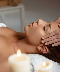 Woman receiving a relaxing facial massage with candles in the foreground