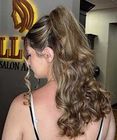 Woman with long wavy brown hair in a salon, viewed from behind.
