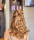 Blonde wavy half-up hairstyle with a twisted bun, viewed from behind in a salon.
