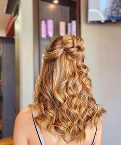 Blonde wavy half-up hairstyle with a twisted bun, viewed from behind in a salon.