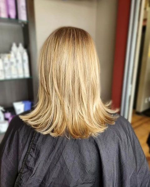 Blonde shoulder-length haircut with soft layers, viewed from behind in a salon chair.