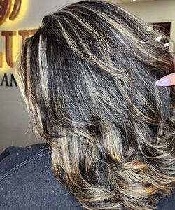 Layered wavy brown hair with blonde highlights, styled in a salon close-up.