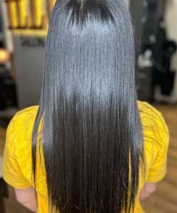 Person with long, straight dark hair wearing a bright yellow top, shown from behind.
