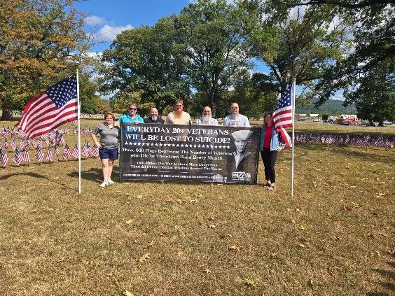 Group of people holding a banner with American flags in a field.