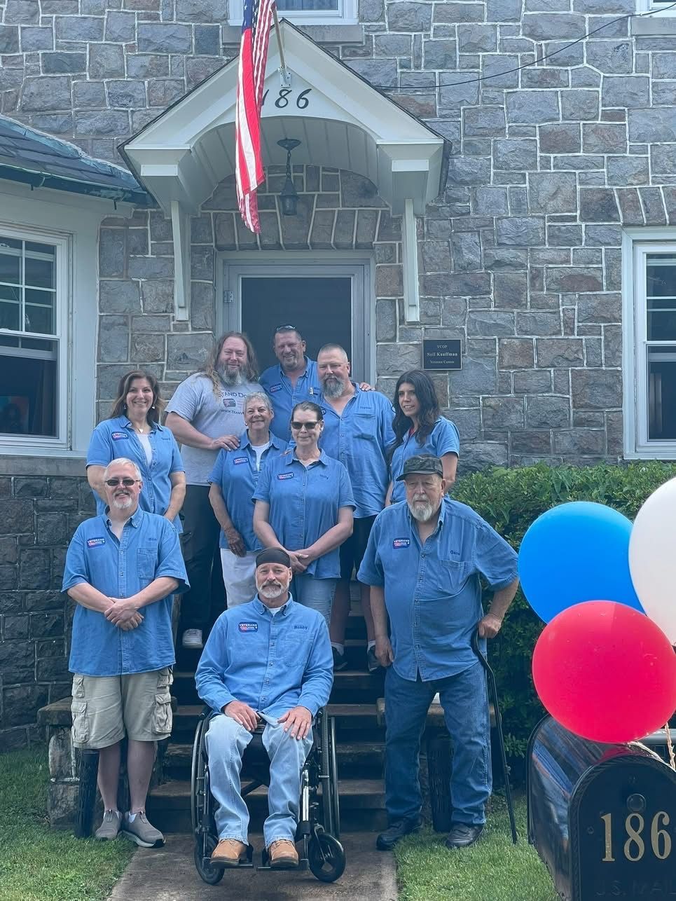 Group of people in blue shirts stand outside a stone building with an American flag.