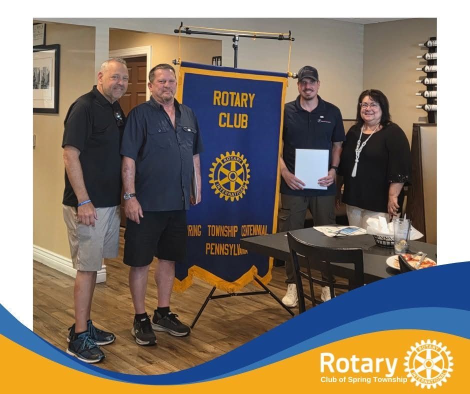 Four people pose in a room with a Rotary Club banner.