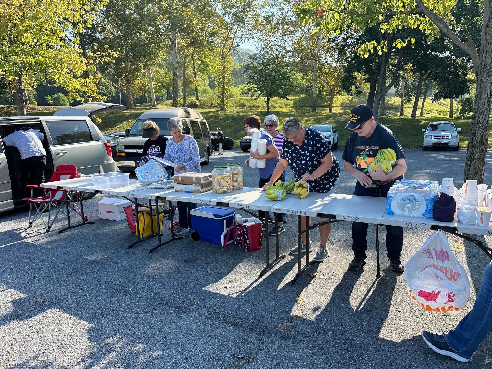 People at an outdoor picnic, setting up food on tables in a parking lot.