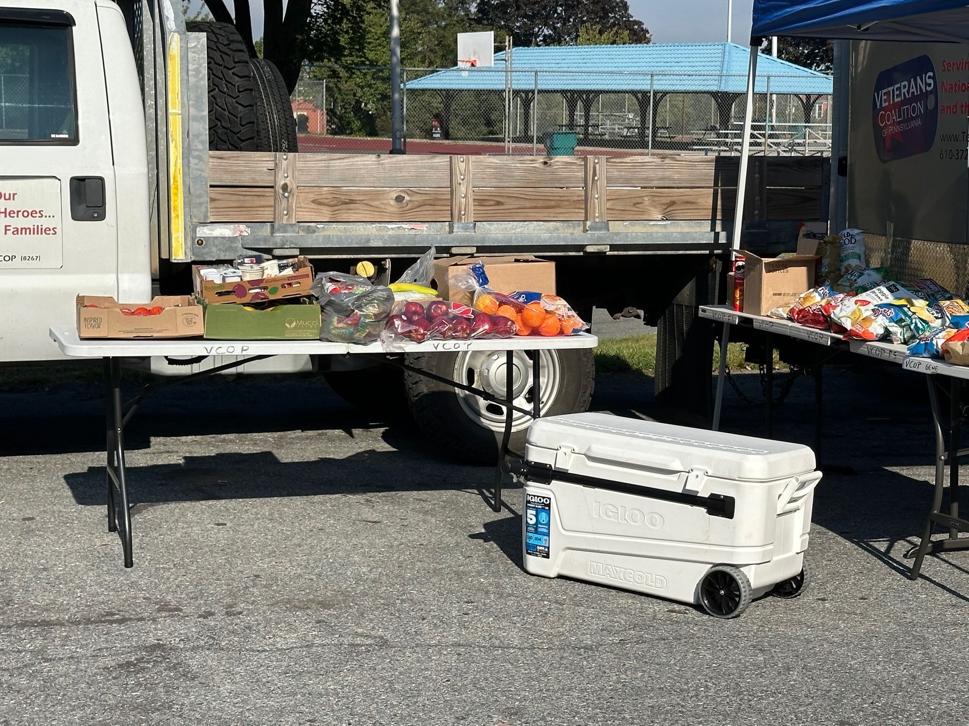 Truck with tables laden with food, cooler nearby; outdoor setting.