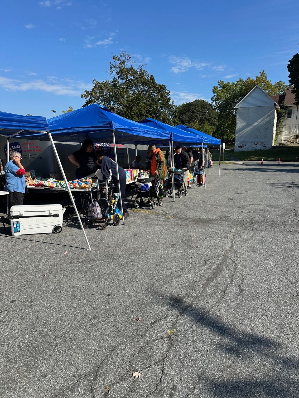 Outdoor market with blue canopy tents and people browsing goods under a clear sky.