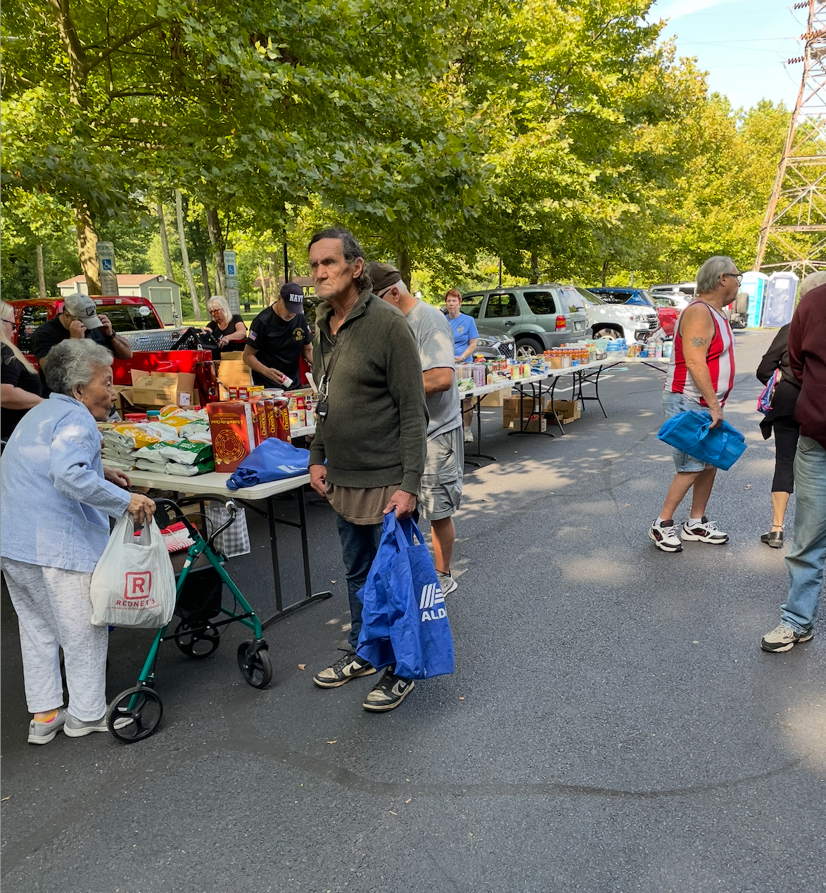 People shopping at an outdoor market, various items on tables, some people holding bags.